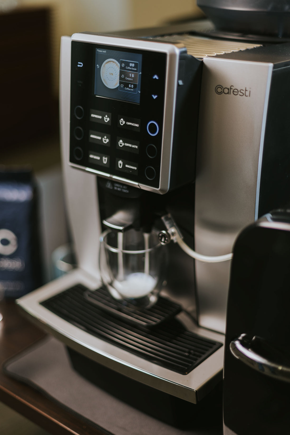 Cafesti Grande automatic coffee machine making a milk-based coffee drink- image showing the frothed milk dispensed into a glass cup